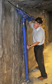 Peter Russell stands in a simulated mining tunnel beside a mining drill.